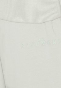 Spodnie dresowe w jasnoszarym materiale z prążkowanym paskiem w talii. Na nogawce znajduje się subtelne logo „JOHN RICHMOND” w tonacji dopasowanej do koloru materiału.