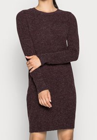 Bordeaux stickad klänning med långa ärmar, rund halsringning och en figurnära siluett. Mjuk textur med ett subtilt melerat mönster genom hela plagg.
