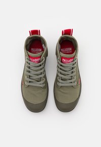 Scarpe alte verde oliva con lacci grigi e punte di gomma. Marchio rosso sulla linguetta e sull'etichetta laterale. Tessuto texture e design robusto.