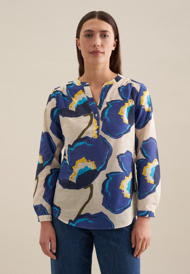 Blusa floreale realizzata in tessuto leggero, con grandi fiori blu e accenti gialli e verdi, apertura con bottoni e maniche lunghe.