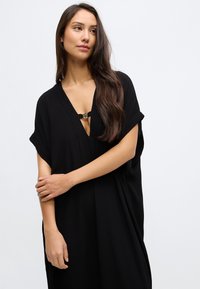 Fekete ruha, könnyű anyagból készült, mély V-nyakú, rövid ujjú, fémszerkezetes kapoccsal a mellrészen.