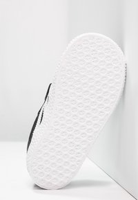 Svart sneaker med en texturerad vit gummisula. Har ett slätt ovansidan material och en rundad tådesign. Sidologga som accent.