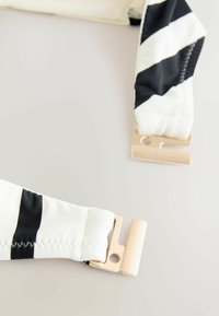 Tirantes de tela a rayas blancas y negras con textura suave y cierres de metal en tono dorado. Presenta costuras a lo largo de los bordes.