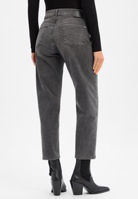 Jeans en denim gris à taille haute, cinq poches et un patch logo en cuir à l'arrière. Associés à des bottines à talons noires.