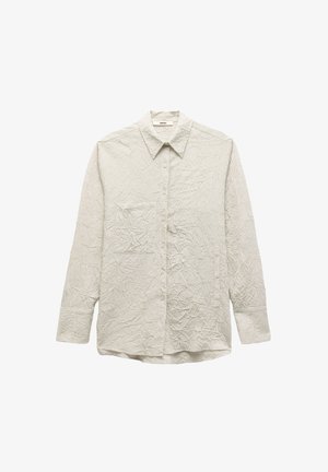 Camicia chiara a maniche lunghe con texture stropicciata, dotata di una tasca sul lato sinistro del petto e colletto classico. Motivo a righe verticali.