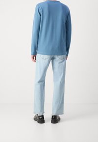 Blaues Langarmshirt, helle Jeans und schwarze Schuhe. Einfaches Design, weicher Stoff, lässige Passform mit sichtbaren Nähten und Taschen. 