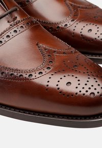 Scarpe eleganti in pelle marrone con dettagli brogue. Presentano motivi perforati, una finitura liscia e una suola scura e robusta.