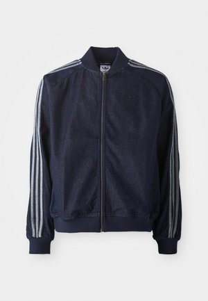 Veste en denim bleu marine avec fermeture éclair à l'avant, poignets côtelés et trois rayures blanches le long de chaque bras. Comprend un petit logo sur la poitrine.