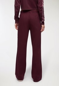 Burgundowe spodnie o szerokiej nogawce, wykonane z miękkiego materiału, z elastycznym pasem i gładką fakturą, zaprojektowane z myślą o komforcie i swobodzie ruchów.
