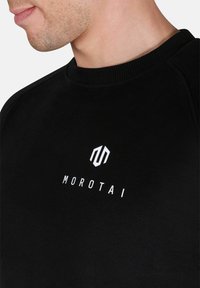 Sudadera negra con cuello redondo y puños acanalados, que presenta un logo en blanco de "Morotai" y un ícono geométrico en el pecho.