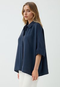 Marineblauwe, oversized blouse met een kraag, korte mouwen en knoopsluiting. Glad materiaal met een relaxed, gedrapeerd model.