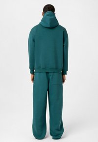 Teal sweatshirt met capuchon en wijde broek, gemaakt van zacht materiaal. Kenmerkt zich door een achterzak op de broek. Eenvoudig ontwerp, geen patronen.