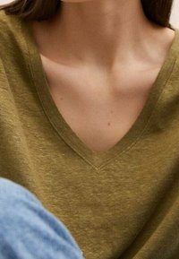 Olijfgroene v-halstrui gemaakt van zachte stof; heeft een relaxte pasvorm en een subtiele textuur. Blauwe denim is zichtbaar en toont een casual stijl.