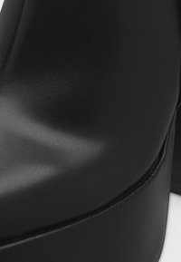 Κοντινό πλάνο απαλού μαύρου δέρματος με λεπτομερείς ραφές κατά μήκος της άκρης, που δείχνει υφή και καμπύλη επιφάνεια.