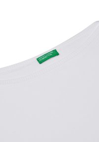 Biała bawełniana koszulka z okrągłym dekoltem, z zieloną metką "United Colors of Benetton" blisko kołnierza. Gładka faktura.