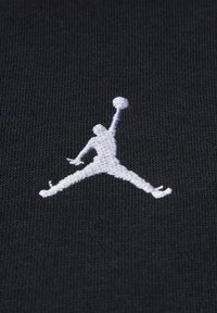 Il tessuto nero presenta un logo Jumpman ricamato in bianco. La texture è liscia con una leggera costina, che mette in risalto la silhouette e i dettagli del logo.