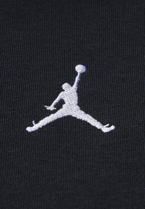 Crni materijal sadrži bijelu izvezenu Jumpman oznaku. Tekstura je glatka s finim rebrastim uzorkom, naglašavajući siluetu i detalje oznake.
