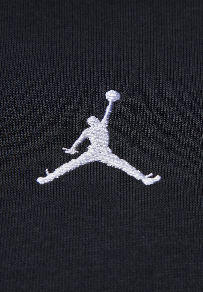 Un tissu noir présente un logo Jumpman brodé en blanc. La texture est lisse avec un fin ribbing, mettant en valeur la silhouette et les détails du logo.