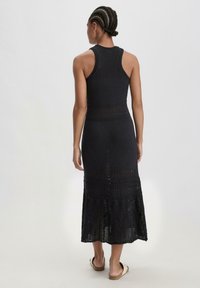 Abito maxi black all'uncinetto senza maniche con un corpetto aderente e un orlo svasato, caratterizzato da motivi dettagliati e una trama aperta.