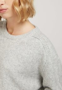 Pull en tricot gris clair avec un col rond, une texture douce et de délicats détails aux épaules avec de petites découpes.