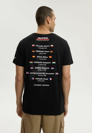 Mężczyzna w czarnej koszulce wymienia daty i lokalizacje Mistrzostw Świata Super Enduro 2025-2026 w europejskich miastach z flagami.