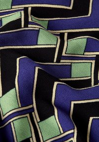 Fabric with a geometric pattern featuring purple, green, and black shapes outlined in beige. Soft texture with subtle sheen.