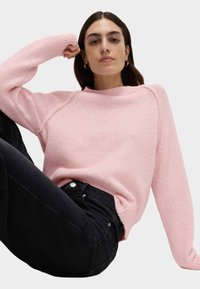 Maglione rosa a maglia con polsini e orlo a coste, caratterizzato da una vestibilità comoda e scollo rotondo, abbinato a jeans scuri.