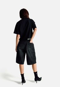 Černé tričko s krátkými rukávy doplněné černými džínovými šortkami s kapsami na cargo a jemným vzorem, doplněné černými vysokými podpatky.