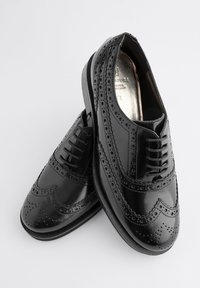 Čierne kožené topánky so vzorom wingtip, zdobené perforáciami, hladkým povrchom, plochou podrážkou a klasickým šnurovaním.