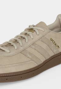 Baskets Adidas Spezial beiges avec tige en daim, bandes texturées, marquage doré, lacets beiges et semelle en caoutchouc marron.