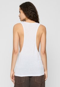 Hvid ærmeløs tanktop med en lav scoop ryg, der har en afslappet pasform og blødt stof. Kanten er buet, hvilket giver en afslappet silhuet.