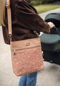 Béžová kabelka přes rameno s květinovými vzory v růžové a bílé barvě. Vyrobená z hladkého materiálu, obsahuje kapsu na zip a nastavitelný popruh.