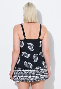 Vestido de baño negro con patrones espirales y florales en blanco. Tirantes ajustables y un dobladillo texturizado presentan diseños contrastantes.