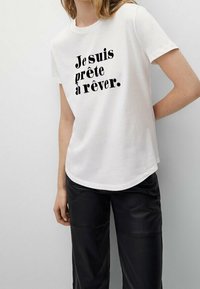 White cotton t-shirt with a crew neck and short sleeves, featuring black text: “Je suis prête à rêver.” Smooth texture, relaxed fit.