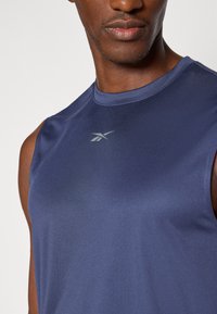 Haut de sport sans manches bleu marine avec une texture lisse, arborant un logo subtil en gris clair, conçu pour le confort et le mouvement.