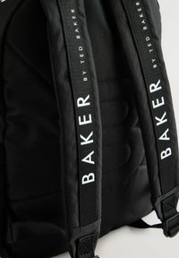 Schwarzer Rucksack mit gepolsterten Schultergurten und weißer Markenkennzeichnung. Texturiertes Material und gesteppte Rückenplatte für zusätzlichen Komfort.