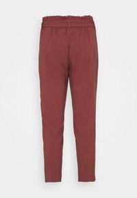 Pantalon taille haute, fuselé, de couleur rouille avec une ceinture élastique et des passants, présenté sur un fond blanc uni.