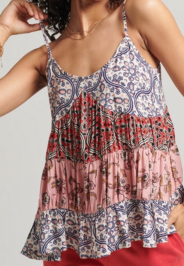Femme portant un haut sans manches à motifs multicolores superposés avec fines bretelles et un pantalon rouge, montrant la taille et le bras levé.