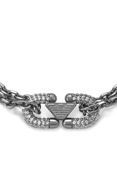 Gros plan sur le fermoir d'un collier à chaîne en argent décoré de petits cristaux transparents et d'un détail central en forme de logo triangulaire.