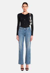 Body a maniche lunghe nero con design a punto croce e bottoni argentati, abbinato a jeans dritti blu chiaro e sandali neri con tacco.