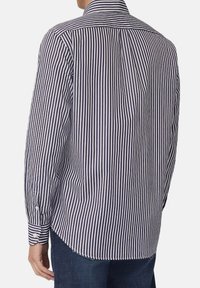 Maglietta a righe blu navy e bianca con maniche lunghe e colletto, dotata di polsini con bottoni e orlo curvo. Tessuto texturizzato visibile.