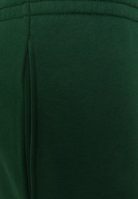 Tissu vert foncé présentant une surface lisse et texturée avec un design ajusté et des détails de couture visibles sur le côté.