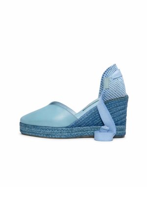Zapato espadrille cuña de color azul claro con suela trenzada de yute y lazo para atar en el tobillo sobre fondo blanco.