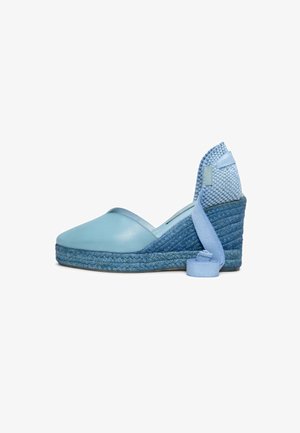 Zapato espadrille cuña de color azul claro con suela trenzada de yute y lazo para atar en el tobillo sobre fondo blanco.