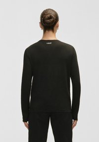 Long-sleeve black shirt made from a soft fabric, featuring a round neckline and a small white "casall" logo at the back.