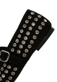Botín negro de ante hasta el tobillo con hebilla metálica, que presenta filas de rhinestones circulares en el costado, suela plana y diseño de punta afilada.