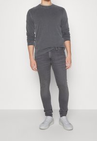 Camiseta gris de manga larga y jeans gris ajustados, combinados con zapatillas blancas. El atuendo presenta un cuello redondo y una textura sutil.