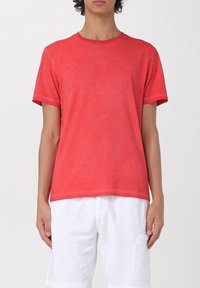 T-shirt corta rossa in cotone con collo rotondo e discreto dettaglio del logo sul petto, abbinata a pantaloni cargo bianchi.