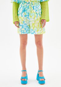 Szorty w jasnoniebieskim i zielonym kolorze z abstrakcyjnym wzorem, z elastycznym pasem i sznurkiem do regulacji. Zestawione z żywymi niebieskimi platformami.