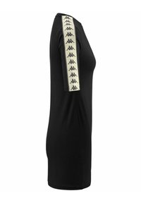 T-shirt nera con una silhouette attillata, caratterizzata da una larga striscia color crema sulla manica sinistra stampata con piccoli loghi neri. Maniche corte, collo girocollo.